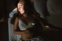 Зверху молода чуттєва жінка в білому мереживний бюстгальтер з барвистою веселкою з закритими очима, спить в ліжку вранці — стокове фото