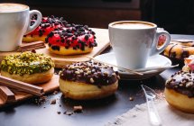 Ciambelle varie con guarnizioni dolci e barrette di cioccolato composte con tazza di cappuccino sul tavolo nero — Foto stock