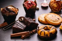 Vários donuts com coberturas doces e barras de chocolate compostas com xícara de cappuccino na mesa preta — Fotografia de Stock