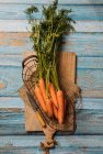Верхний вид собранной спелой моркови с зеленой листвой, помещенной на раскройную доску на деревянном столе — стоковое фото