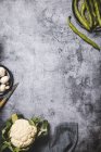 Draufsicht auf organische grüne Schoten auf rundem Metalltablett mit Pilzen und Blumenkohl auf grunge-grauer Oberfläche — Stockfoto
