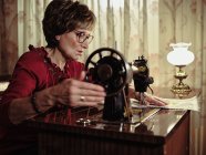 Senior dame dans les lunettes en utilisant une machine à coudre rétro pour créer une serviette de lin dans une chambre confortable à la maison — Photo de stock