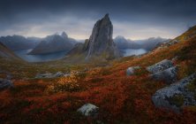 Segla montanha localizada no vale gramado perto da bacia calma contra o céu nublado escuro na ilha de Senja, Noruega — Fotografia de Stock
