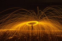 Довгий силует невизначеної людини, що обертається пекучою паличкою, що випромінює блискітки під час танців з вогнем вночі — стокове фото