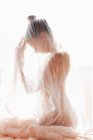 Вид збоку анонімної гола модель, вкрита прозорою плісированою тканиною завіси проти яскравого сонячного світла — стокове фото