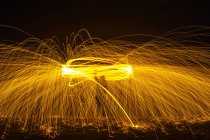 Long exposure silhouette of unrecognizable person spinning burning stick emitting sparkles while dancing with fire at night — Stock Photo