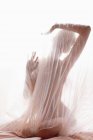 Modelo nu anônimo coberto com tecido plissado transparente de cortina contra a luz solar brilhante — Fotografia de Stock