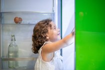 Bambina in pigiama party in cerca di snack all'interno del frigorifero aperto di notte in cucina a casa — Foto stock
