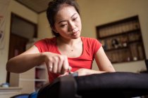 Joven mujer asiática étnica con anillo en el dedo meñique tornillo giratorio mientras instala mango en la silla en casa - foto de stock