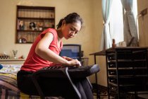 Low angle of ethnic lady sitting on bed and checking soft seat with handles while assembling chair at home — Stock Photo