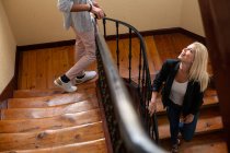 From above blonde female smiling and communicating with crop anonymous boyfriend while walking down wooden staircase at home together — Stock Photo