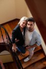 Мужчина и женщина улыбаются перед камерой и обнимаются, стоя дома на лестнице. — стоковое фото