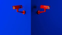 Red surveillance camera on blue background monitoring people on the street. Camera to search for quarantine offenders caused by Coronavirus — Stock Photo