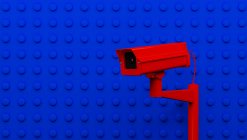 Red surveillance camera on blue background monitoring people on the street. Camera to search for quarantine offenders caused by Coronavirus — Stock Photo