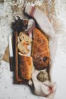 From above rustic composition with aromatic bread loaves on board with linen towel and knife on shabby surface — Stock Photo