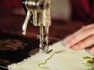 Señora mayor en gafas utilizando la máquina de coser retro para crear servilleta de lino en la habitación acogedora en casa - foto de stock