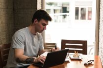 Freelancer sitting at cafe table and browsing laptop — Stock Photo