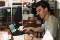 Freelancer seduto al tavolo del caffè e portatile di navigazione — Foto stock