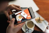 Зверху анонімний молодий чоловік використовує смартфон, щоб сфотографувати чашку кави і смачний салат в кафе — стокове фото