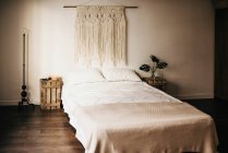 Decoración de macramé vintage colgando en la pared sobre una cama cómoda en el acogedor dormitorio en casa - foto de stock