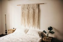 Vintage macrame decoration hanging on wall over comfortable bed in cozy bedroom at home — Stock Photo