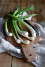 Bando de cebolinhas maduras colocadas em tábua de corte de madeira e guardanapo de pano em mesa rústica na cozinha — Fotografia de Stock