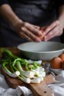 Cropped woman hands breaking eggs in a bowl with bunch of fresh scallions and mushrooms placed on cutting board near poppy seeds — Stock Photo