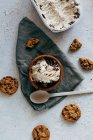 Top view of delicious oatmeal cookies and plastic spoon placed around ceramic bowl of sweet ice cream and cloth napkin on plaster surface — Stock Photo