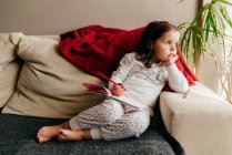 Cute little girl sitting on the couch with a notebook looking for inspiration — Stock Photo