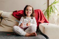 Nettes kleines Mädchen sitzt auf der Couch und lächelt mit einem Notizbuch — Stockfoto