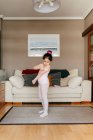 Симпатична маленька дівчинка в світло-рожевому леопарді і колготки готуються, стоячи біля танцювального взуття в затишній вітальні вдома — стокове фото