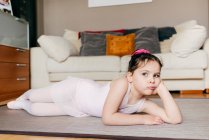 Набридла маленька дівчинка в леопарді лежить на підлозі, дивлячись далеко, відпочиваючи під час репетиції балету вдома — стокове фото