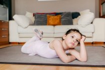 Скучная задумчивая маленькая девочка в трико, лежащая на полу и смотрящая в сторону во время репетиции балета дома — стоковое фото