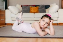 Noioso pensieroso bambina in body sdraiata sul pavimento guardando lontano mentre riposava durante le prove di balletto a casa — Foto stock