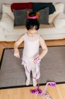 Сверху сосредоточенная милая маленькая девочка в трико и трико, крутящаяся лента во время занятий художественной гимнастикой в уютной гостиной дома — стоковое фото