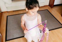 From above focused cute little girl in leotard and tights spinning ribbon during rhythmic gymnastic practice training in cozy living room at home — Stock Photo