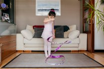 Konzentrierte süße kleine brünette Mädchen in Trikot und Strumpfhosen beim Spinnen Band während rhythmische Gymnastik-Training im gemütlichen Wohnzimmer zu Hause — Stockfoto