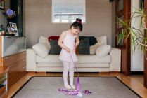 Focused cute little brunette girl in leotard and tights while spinning ribbon during rhythmic gymnastic practice training in cozy living room at home — Stock Photo
