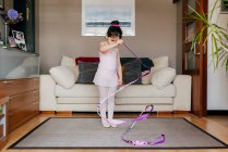 Focused cute little brunette girl in leotard and tights while spinning ribbon during rhythmic gymnastic practice training in cozy living room at home — Stock Photo