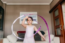 Konzentriert glücklich süßes kleines brünettes Mädchen im Trikot beim Spinnen des Bandes beim rhythmischen Gymnastiktraining im gemütlichen Wohnzimmer zu Hause — Stockfoto