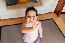 From above little girl with ribbon smiling for camera and waving hand during rhythmic gymnastic training at home — Stock Photo