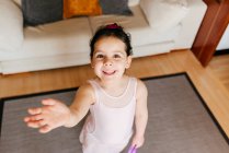 Зверху маленька дівчинка зі стрічкою посміхається для камери і махає рукою під час ритмічної гімнастики вдома — стокове фото
