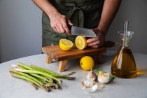 Анонімний чоловічий шеф-кухар нарізає свіжий лимон на дерев'яній дошці, готуючи здорову страву за столом з інгредієнтами для рецепту — стокове фото