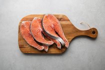 Верхний вид свежих стейков лосося на деревянной доске, приготовленных для вкусного здорового рецепта помещен на мраморный стол — стоковое фото