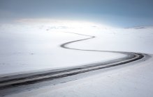 Estrada de campo curvilínea vazia passando por terreno nevado — Fotografia de Stock