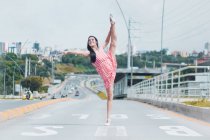 Full body young ballerina smiling and doing splits on empty lane of road while dancing in modern city outskirts — Stock Photo