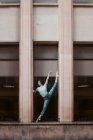Mulher magra de comprimento total em roupas casuais fazendo divisões enquanto se alonga e dança fora do edifício resistido na cidade — Fotografia de Stock