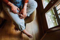 From above anonymous barefoot woman in jeans embracing baby while sitting on chair near window in cozy room at home — Stock Photo