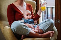 Coltiva la madre con succo e bambino appoggiato sulla sedia — Foto stock