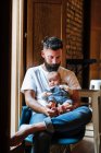 Barbuto padre con bambino seduto vicino alla finestra — Foto stock